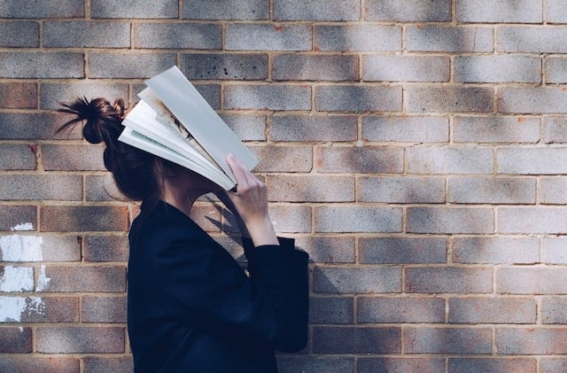 How to avoid distractions while studying online. Image of a lady covering her face with a book 